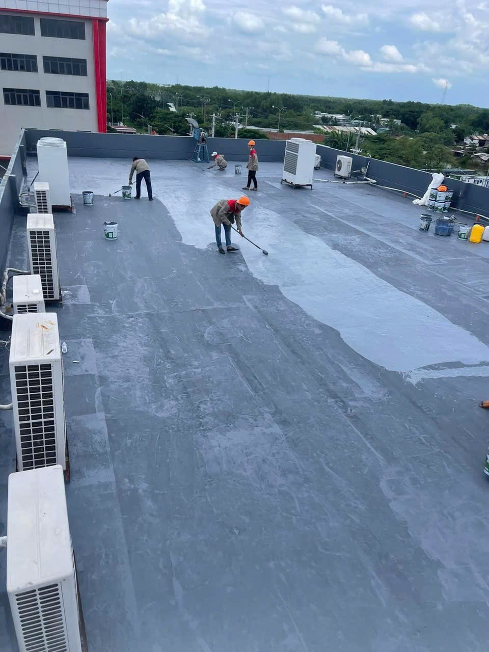 Công nhân đang thi công lớp phủ chống thấm polyurethane trên mái nhà, với thiết bị hiện đại, cho thấy sự chuyên nghiệp và công nghệ tiên tiến trong cải tạo công trình dân dụng.