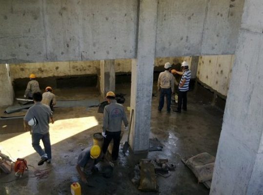 Hình ảnh một đội ngũ kỹ thuật viên chuyên nghiệp đang thi công chống thấm tầng hầm, sử dụng các công cụ và vật liệu hiện đại. Nên có chi tiết về việc sử dụng màng chống thấm hoặc sơn chống thấm, thể hiện sự chuyên nghiệp và cẩn thận trong quy trình thi công