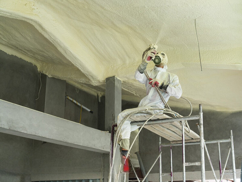 Hình ảnh cận cảnh một công nhân đang sử dụng máy phun bọt PU để xử lý các vết nứt hoặc khe hở trên sàn tầng hầm. Bọt PU đang lấp đầy các khe nứt và hình thành lớp chống thấm chắc chắn