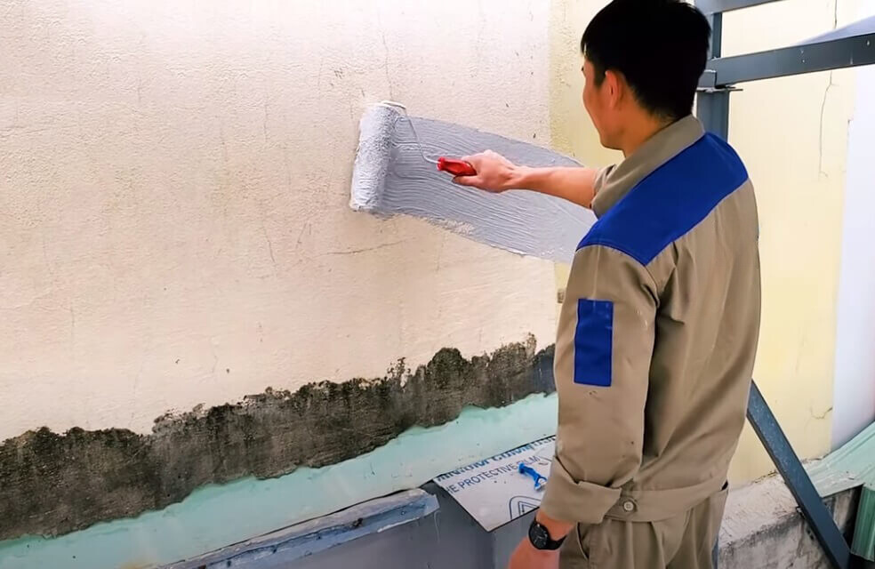 Kỹ thuật viên đang kiểm tra và xử lý vết nứt trên tường ngoại thất của tòa nhà bằng vật liệu chống thấm polyurethane. Hình ảnh minh họa quy trình cải tạo hệ thống chống thấm chuyên nghiệp để bảo vệ kết cấu tòa nhà