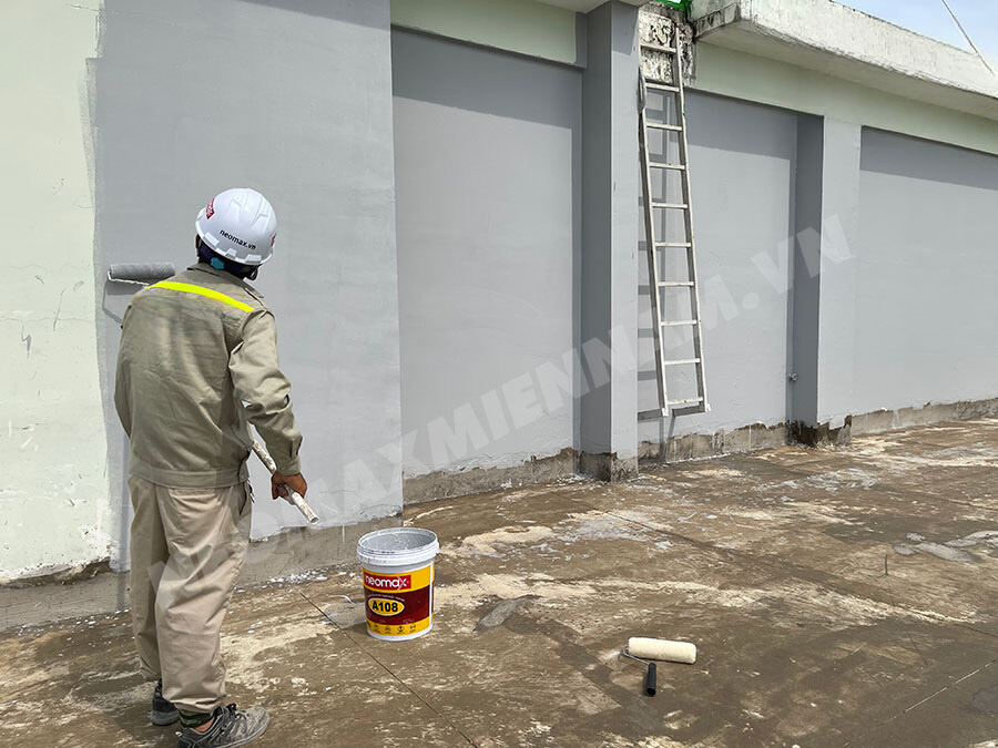 Kỹ thuật viên đang thi công lớp sơn chống thấm trên bề mặt tường ngoài, sử dụng các dụng cụ chuyên dụng như con lăn và cọ. Hình ảnh minh họa quy trình thi công chống thấm tường một cách chuyên nghiệp