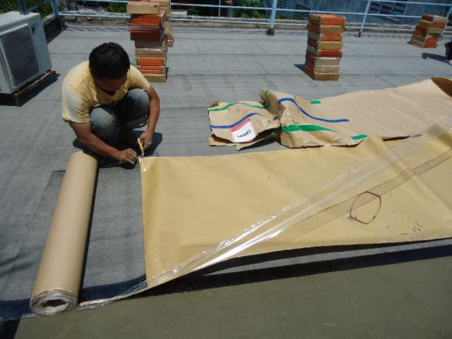 Công nhân dán màng chống thấm tự dính lên tường tầng hầm, thể hiện công nghệ chống thấm hiện đại trong xây dựng công trình lớn.