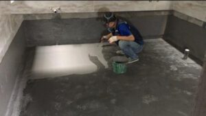 Công nhân đang quét lớp sơn chống thấm trên sàn nhà vệ sinh với dụng cụ chuyên dụng.