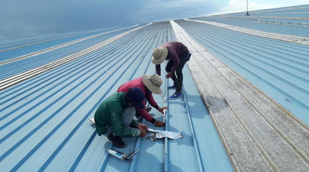 Ảnh kiểm tra và vệ sinh mái tôn: Công nhân đang kiểm tra và làm sạch bề mặt mái tôn để chuẩn bị cho việc chống dột.